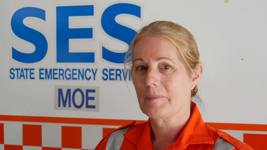 A blonde women with an orange jumpsuit stands in front of an SES Moe sign.