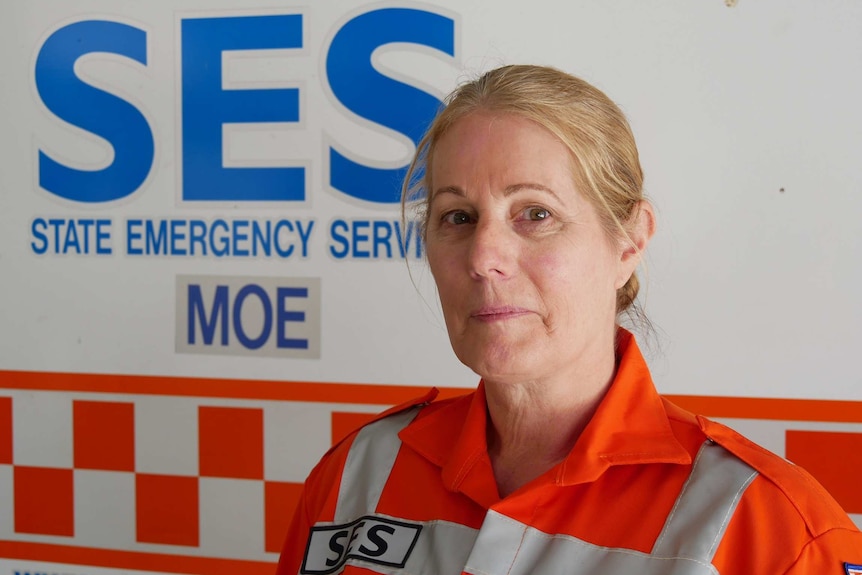 A blonde women with an orange jumpsuit stands in front of an SES Moe sign.