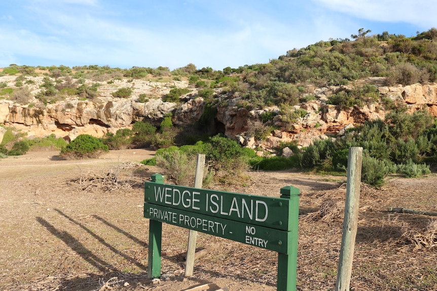 Green sign of Wedge Island and small rocky cliff.