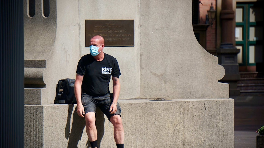 A man stands up wearing a mask in a street.