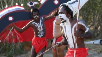 Indigenous dancers wearing white patterned paint perform a dance.