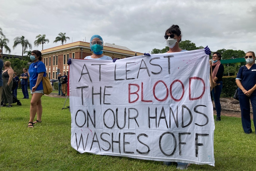 two people wearing masks holding a large white sheet as a sign