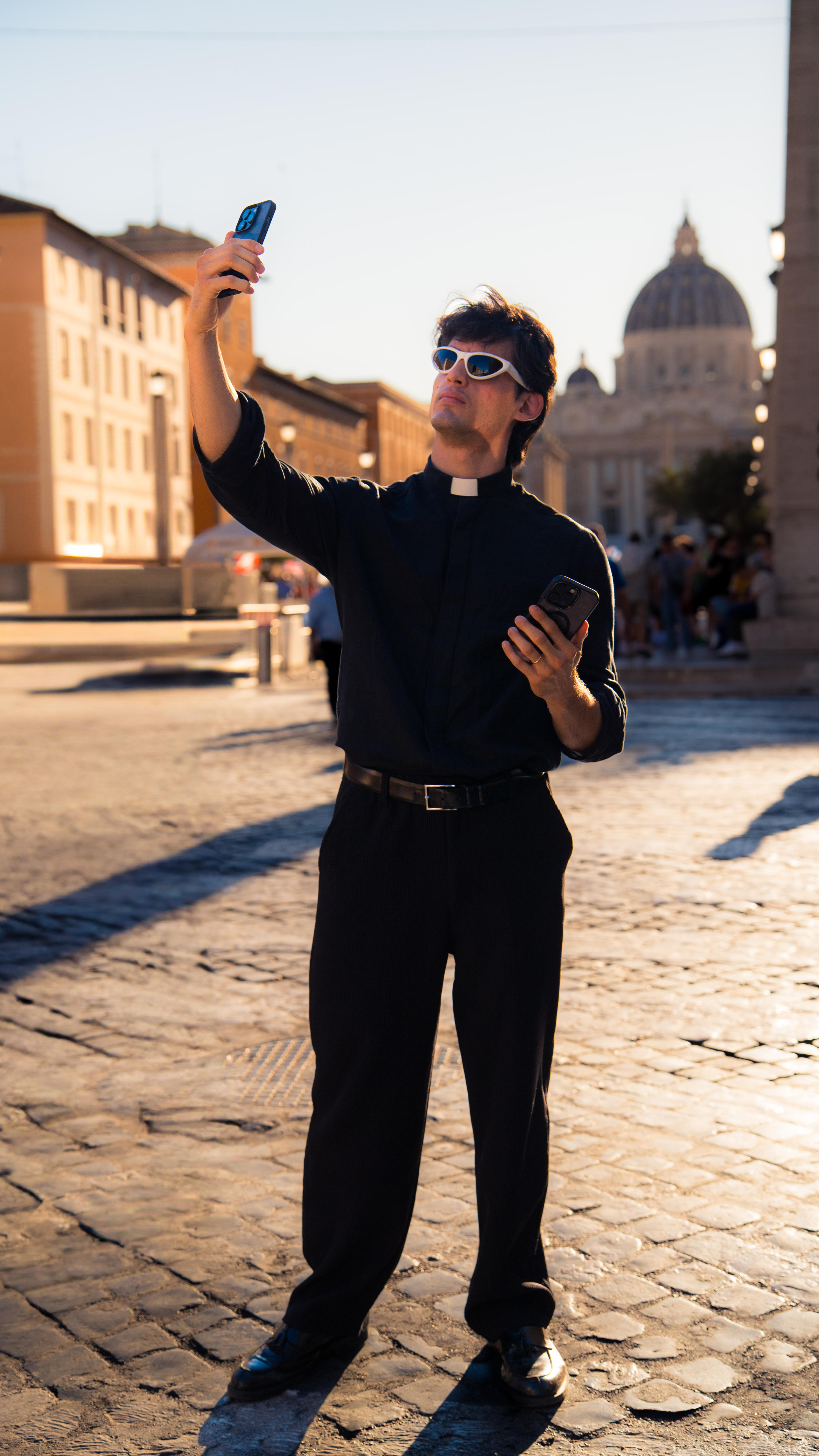 A young man in black clothes and a clerical collar takes a selfie.