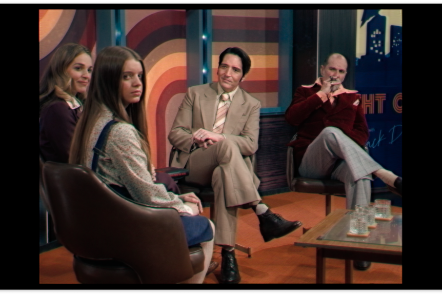 Black bars surround an image of four people in chairs on set of a talk show. A young girl looks directly into the camera.