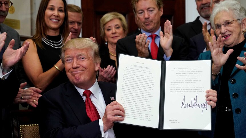 Donald Trump smiles while holding up a signed executive order.