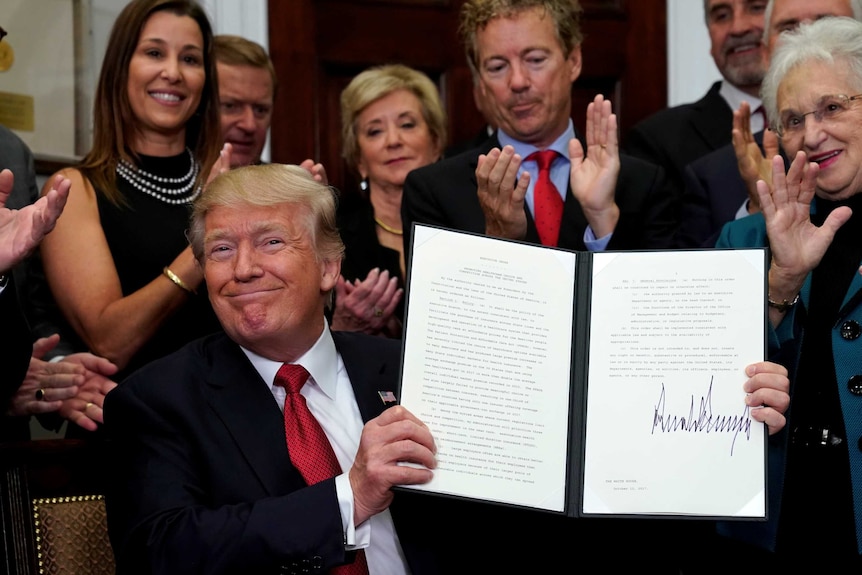 Donald Trump smiles while holding up a signed executive order.