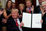 Donald Trump smiles while holding up a signed executive order.