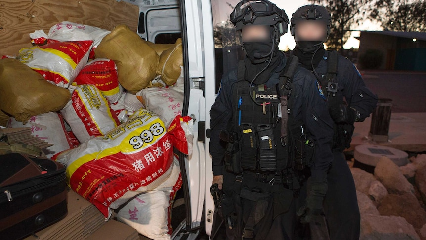 Two AFP officers with faces blurred next to an open van door containing sacks of drugs.