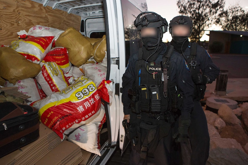 Двама служители на AFP със замъглени лица до отворена врата на микробус, съдържащ чували с наркотици.