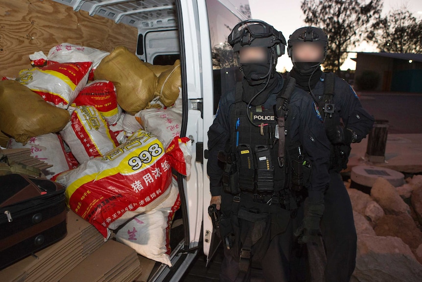 Two AFP officers with faces blurred next to an open van door containing sacks of drugs.