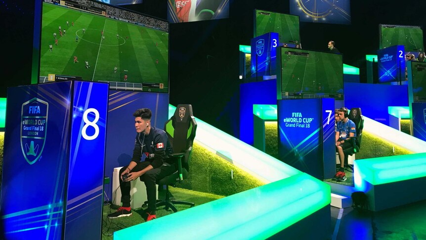 Two players sit in separate booths playing computer games with banners around them