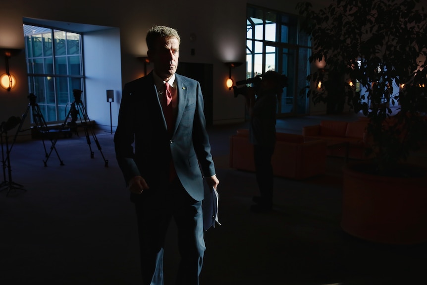 Dan Tehan, with a shadow across his face, walks away from a press conference at parliament house