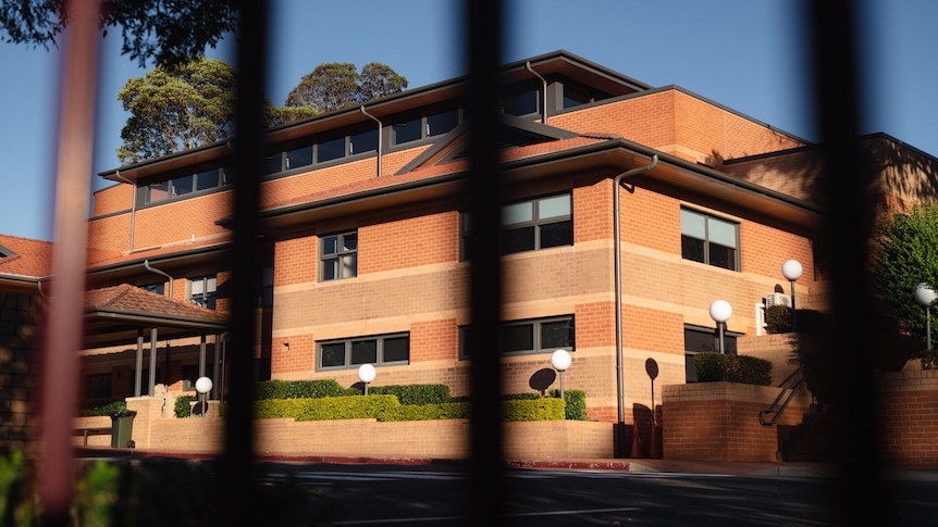 A large brick school building shot from behind bars of the school fence.