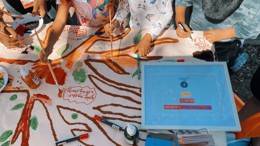 A group of children gather around a table, painting a colourful mural 