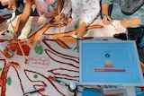 A group of children gather around a table, painting a colourful mural 