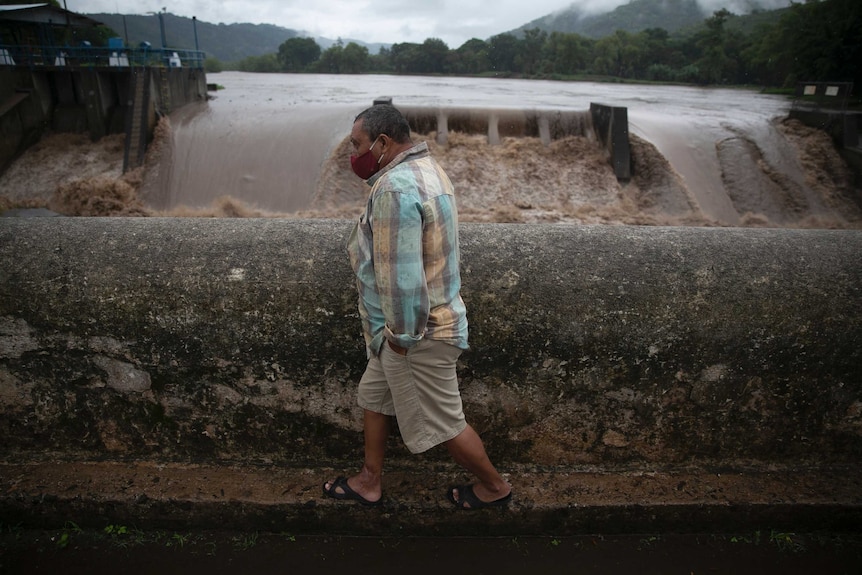 A man walks on a bridge over a river during tropical storm Amanda.