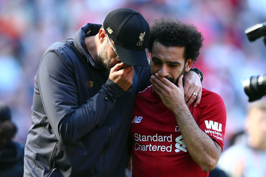 Jurgen Klopp wraps his arm around Mohamed Salah as both hold their hands to their mouths and talk