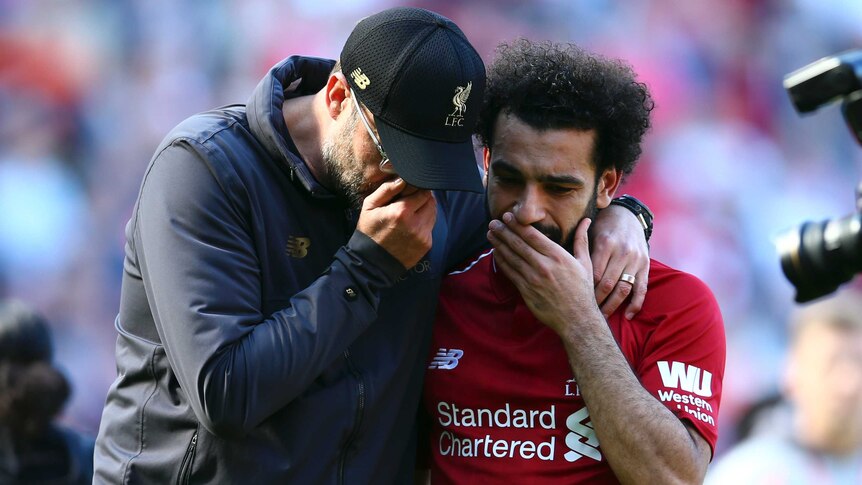 Jurgen Klopp wraps his arm around Mohamed Salah as both hold their hands to their mouths and talk
