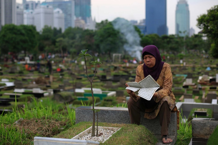 A woman reads the Koran at her husband's grave in a cemetery.