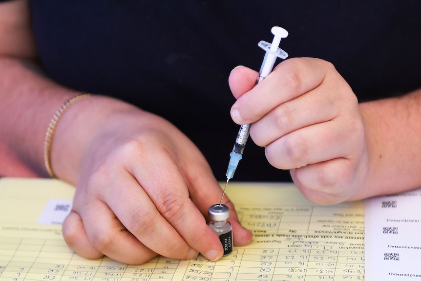 Nurses's hands fill injection of COVID-19 vaccine from a vial. 