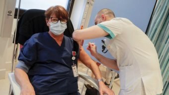 A woman wearing a facemask receives a coronavirus vaccine