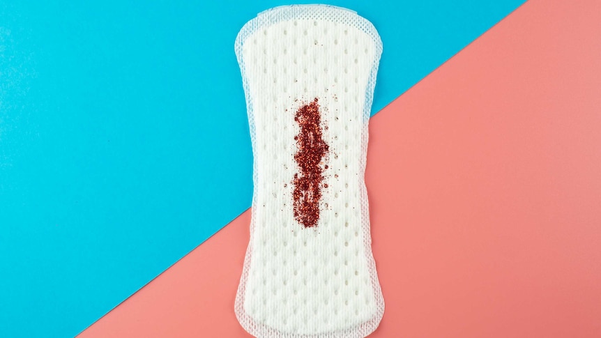 A sanitary pad with red glitter simulating a blood stain on a pink and blue background