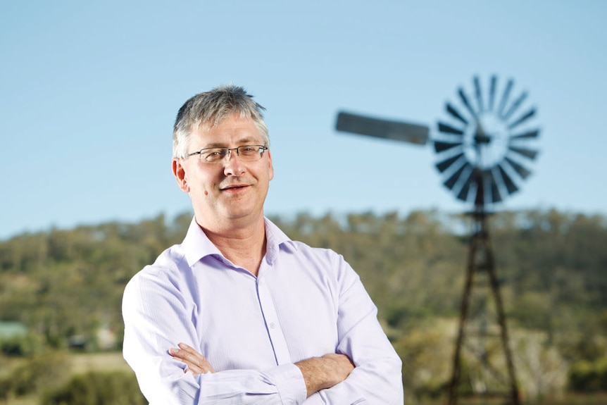A man stands in front of a windmill with his arms crossed