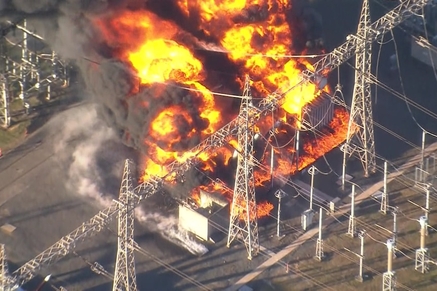 Aerial shot of a big fire burning among poles and wires in a power substation. 