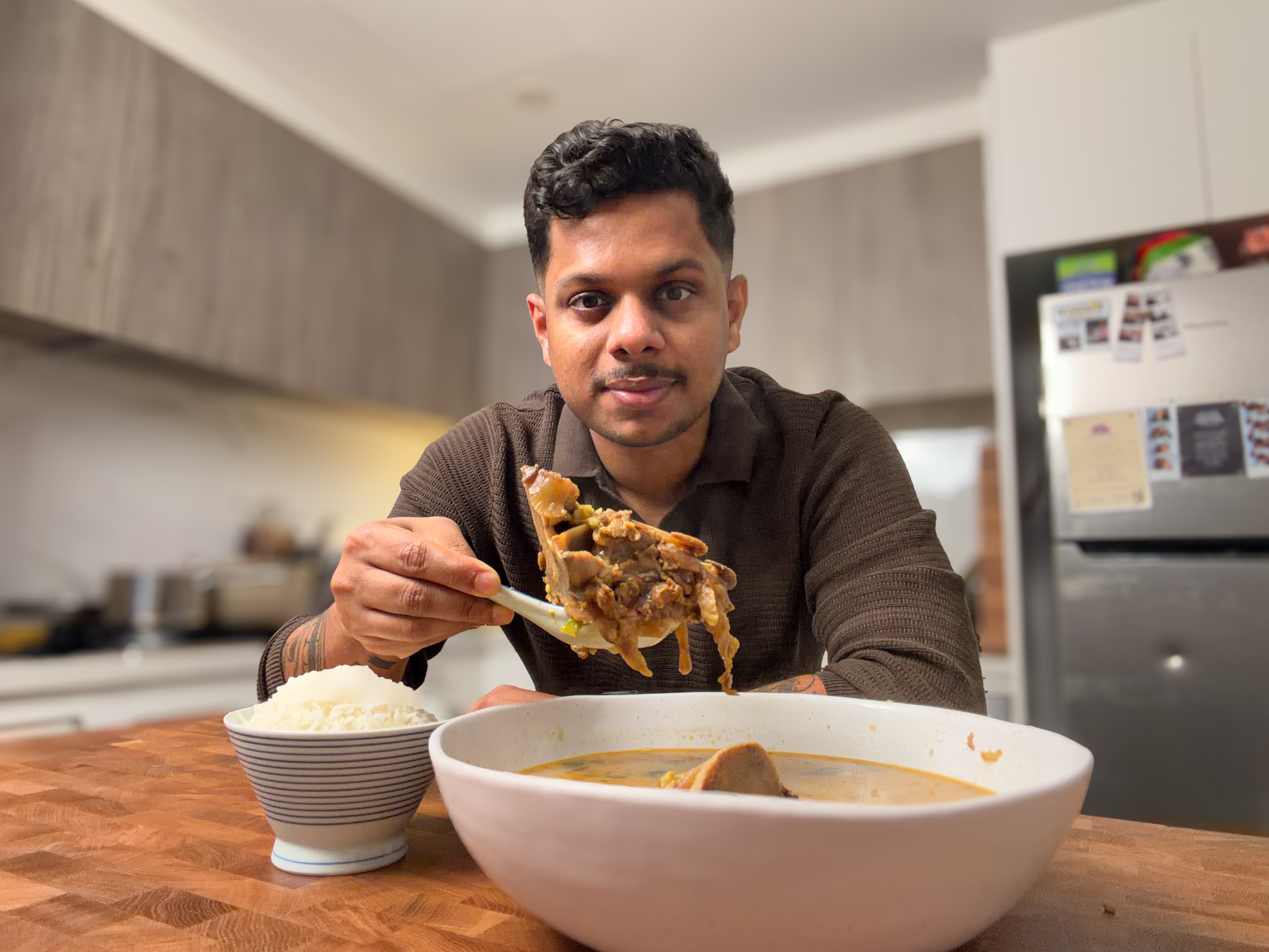 Nip Liyanapathirana sits behind a bowl of his beef-bone soup, holding a large bone up on a spoon.