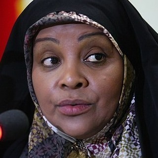 A woman in a head scarf speaks into a microphone.