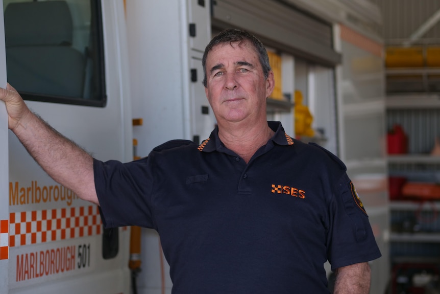 A man with short brown hair leans his arm against an SES truck and looks at the camera