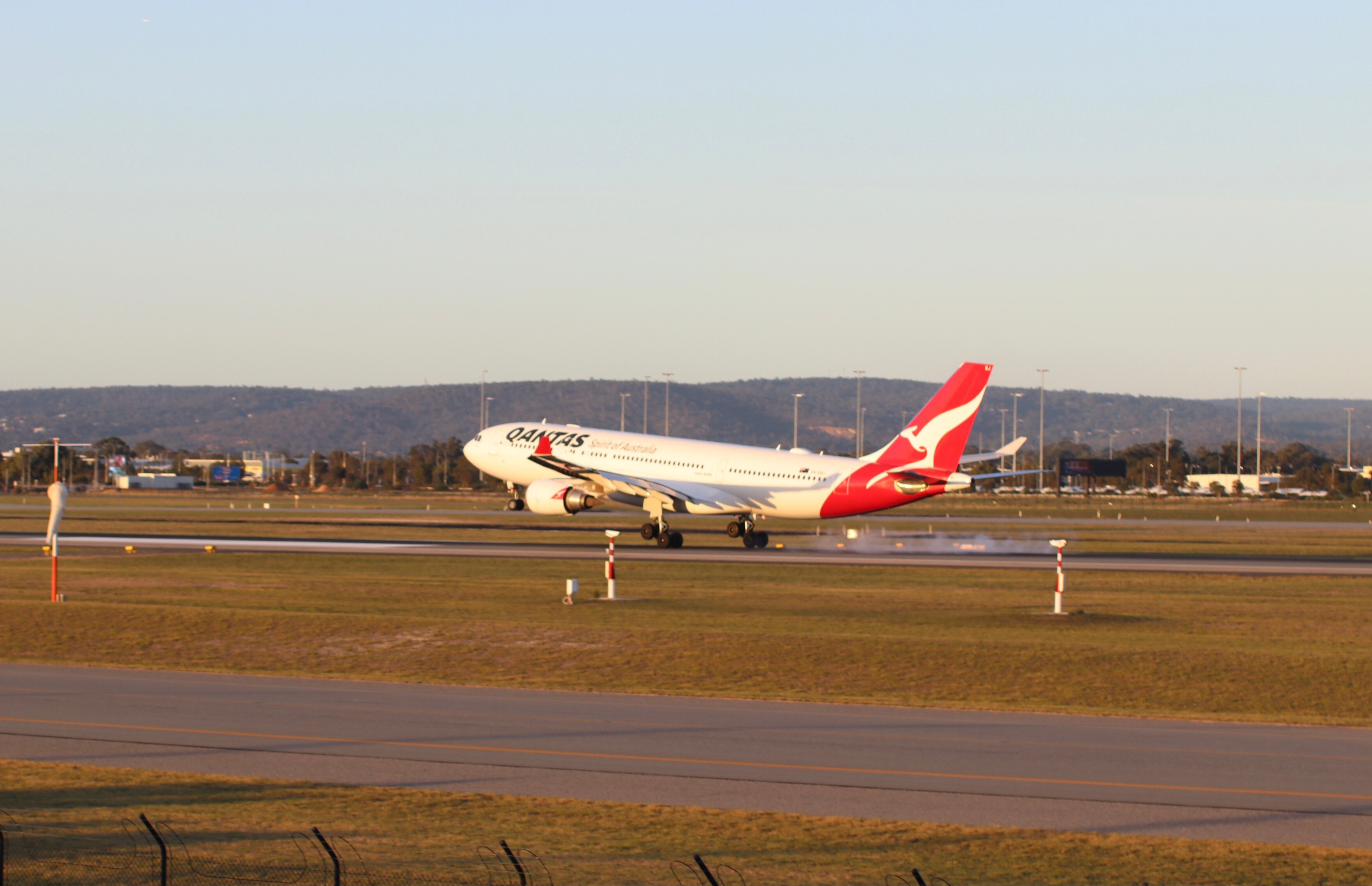 A Qantas aircraft lands on the runway at Perth Airport on a sunny afternoon.