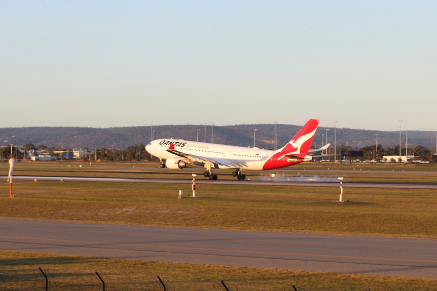A Qantas aircraft lands on the runway at Perth Airport on a sunny afternoon.