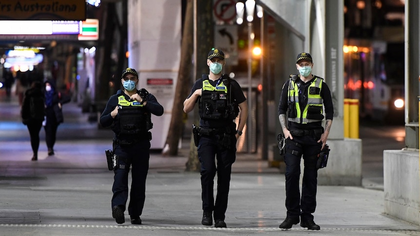 Three protective service officers wearing masks walk down a footpath in Melbourne's CBD.