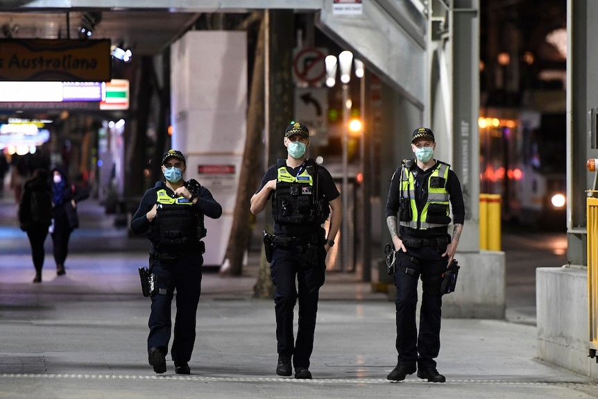 Three protective service officers wearing masks walk down a footpath in Melbourne's CBD.