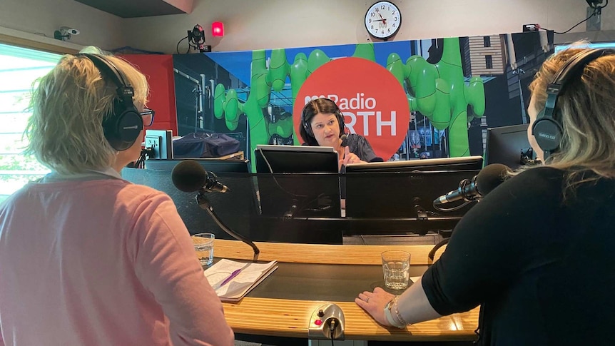 Two women standing with their backs to the camera in the ABC radio studio speaking with the Mornings host
