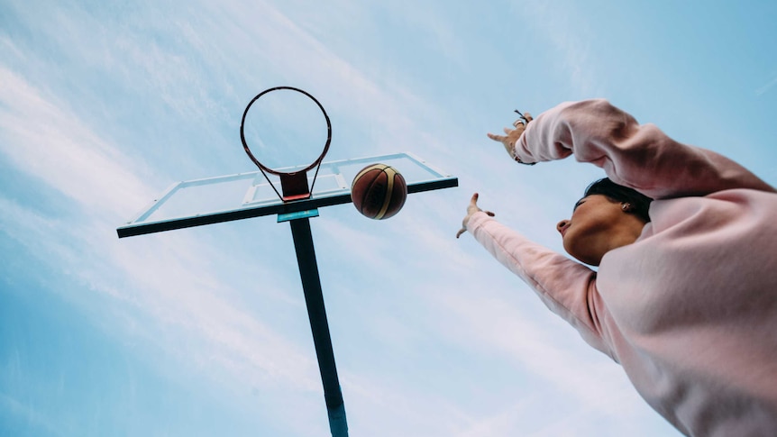 From beneath a basketball ring looking up to it, a woman in a jumper shoots a basketball up towards the ring.