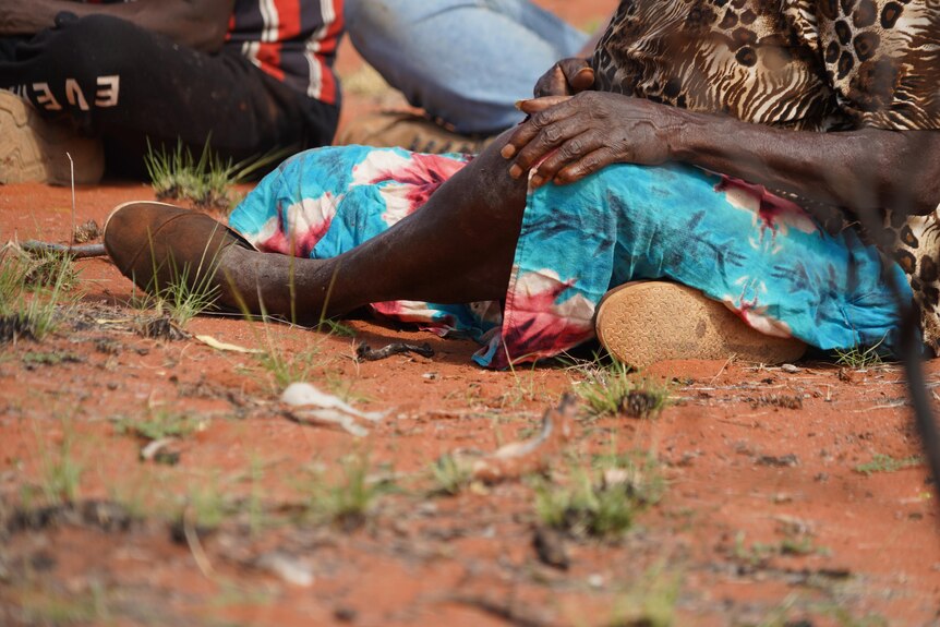 An old Aboriginal woman sits in the red dirt