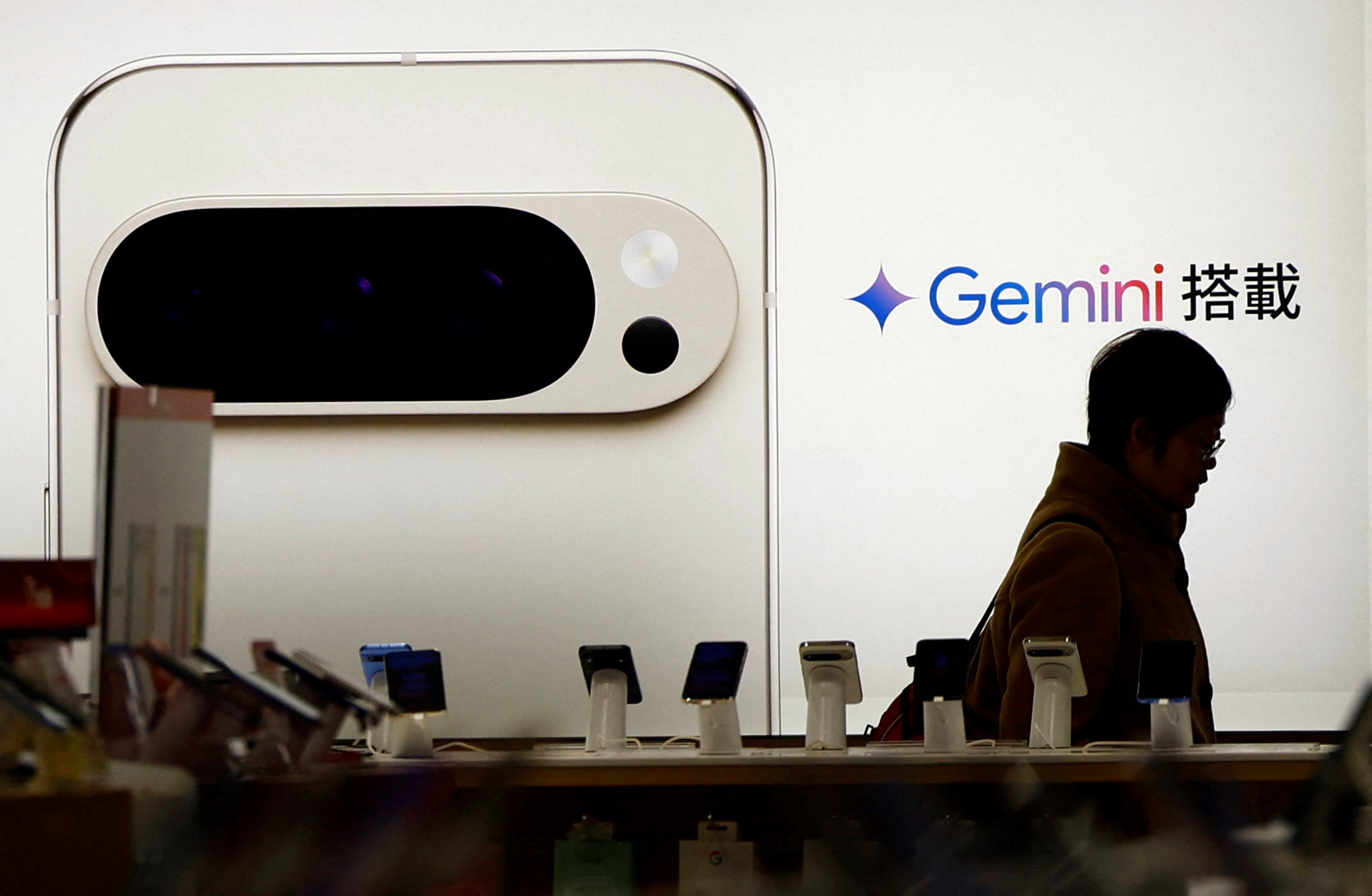 A silhouette of a man is seen in front of a full-wall smartphone ad with the Gemini logo next to it
