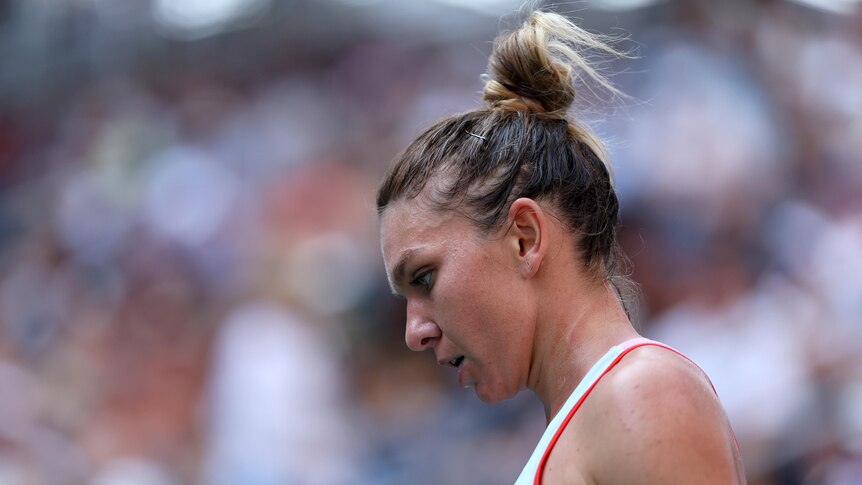 A woman tennis player with her hair in a bun looks defeated