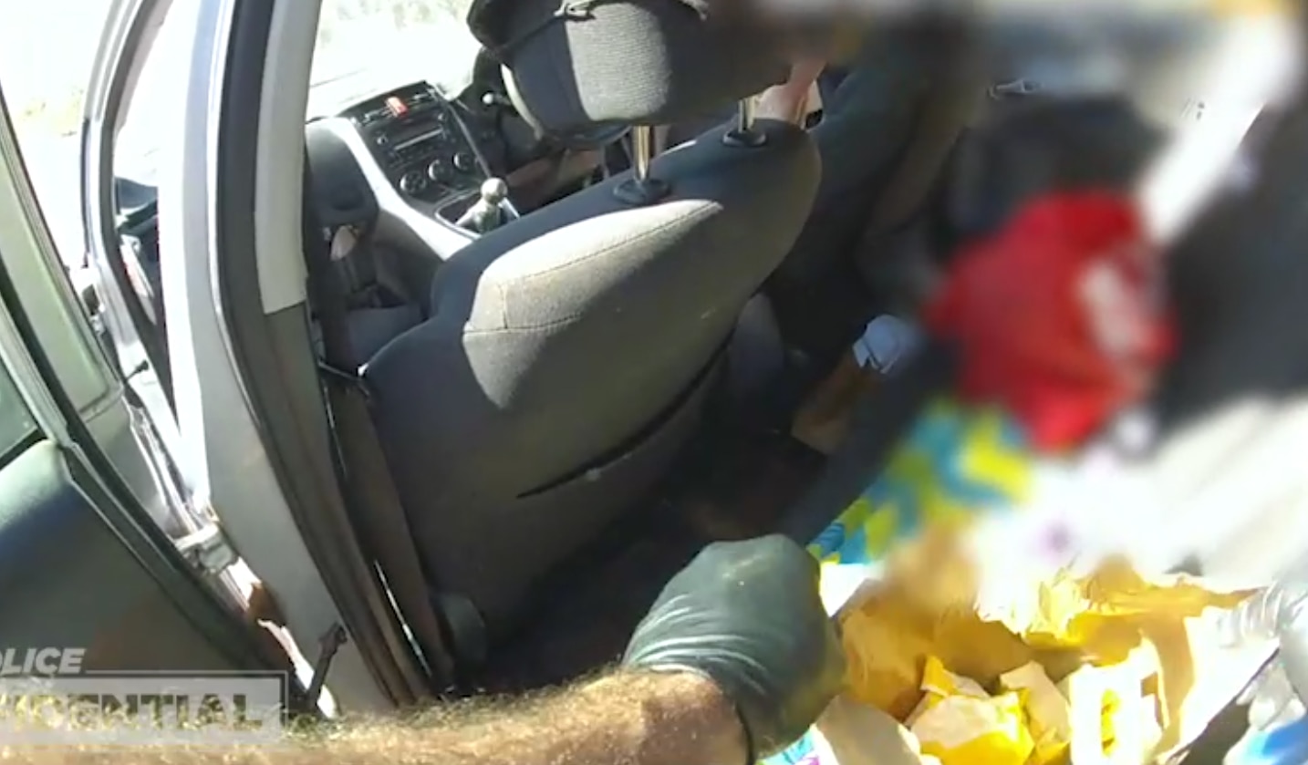 A police officer in gloves searches a car, as seen from a body camera.