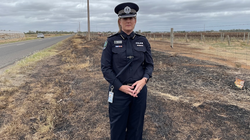 A police officer stands the side of a road on ground scorched by a fire