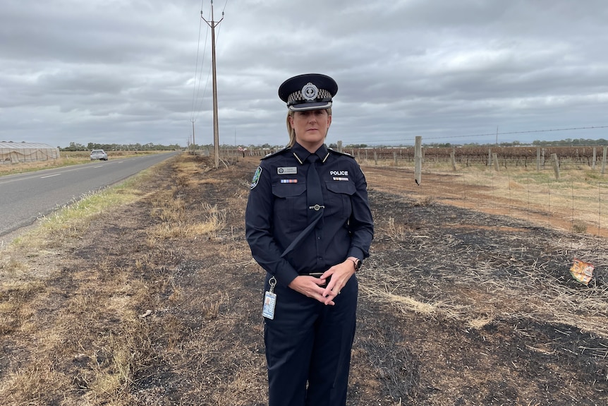 A police officer stands the side of a road on ground scorched by a fire