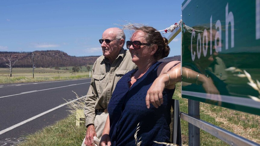 A woman and man looking into the distance with hills behind and a sign saying Coolah