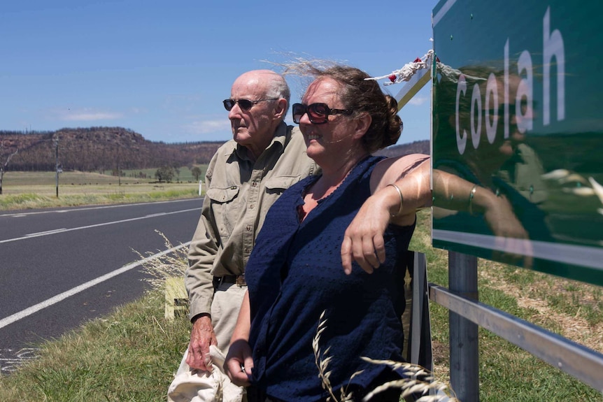 A woman and man looking into the distance with hills behind and a sign saying Coolah