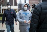 A man walks outside a court room wearing a hoodie reading 'Rebels'