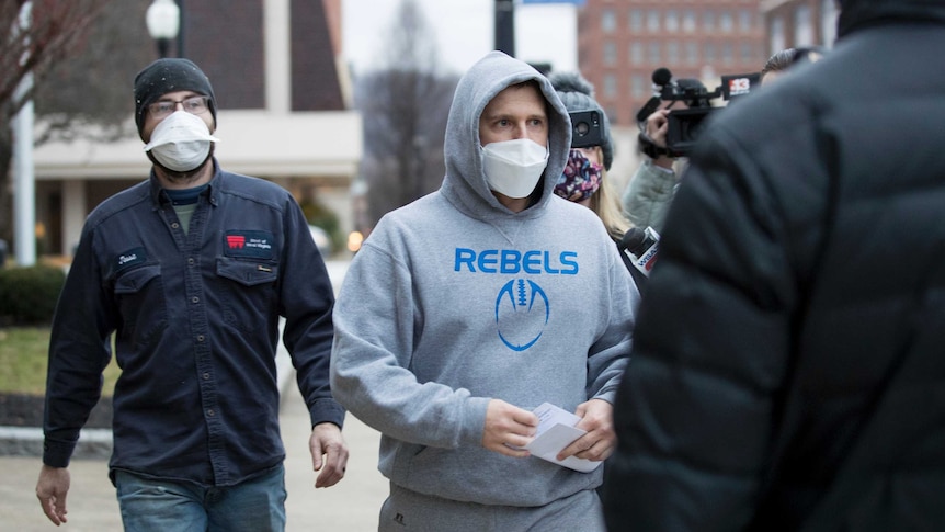 A man walks outside a court room wearing a hoodie reading 'Rebels'