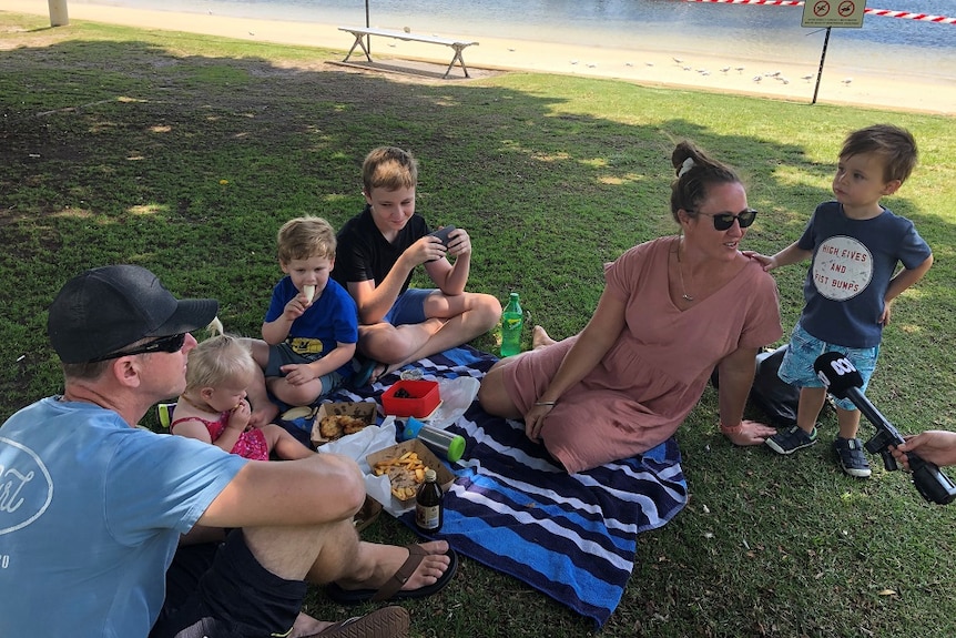 Man, woman and four children having a picnic on the grass at Nelson Bay Foreshore.