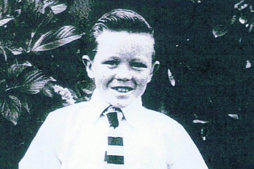 A boy of about  eight, in a school uniform, a black and white picture.