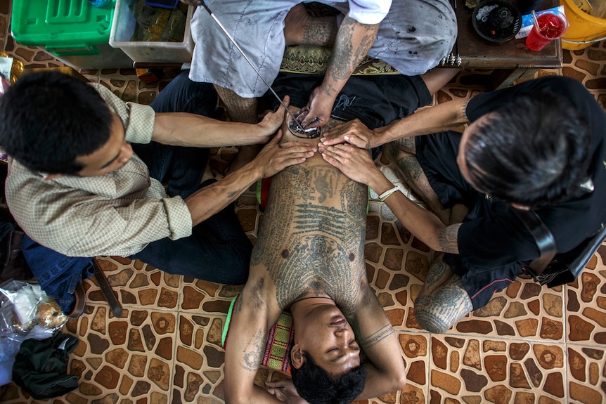 People using a traditional needle to tattoo the body of a man in Thailand.